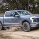 A photo of an electric, Ford F-150 lightning pickup ruck driving on a dusty track.